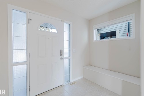 The entryway features a white front door with an arched window and two frosted glass sidelights, light-colored walls, and a built-in bench below a horizontal window - 1135 112 Street, Edmonton, AB - Indoor Photo Showing Other Room