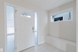 The entryway features a white front door with an arched window and two frosted glass sidelights, light-colored walls, and a built-in bench below a horizontal window - 