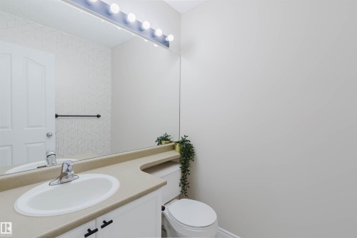 Bathroom featuring a vanity with a light-colored countertop and an integrated sink, a large mirror with overhead lighting, and a toilet - 1135 112 Street, Edmonton, AB - Indoor Photo Showing Bathroom