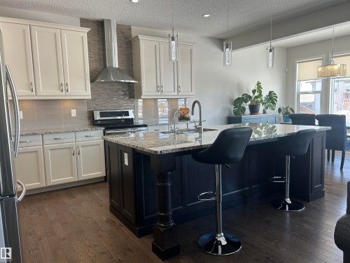 Kitchen featuring light-colored cabinetry, a dark-toned island with a granite countertop, and stainless steel appliances - 5333 21A Avenue, Edmonton, AB - Indoor Photo Showing Kitchen With Upgraded Kitchen