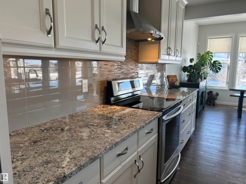 Well-appointed kitchen featuring granite countertops, light-toned cabinetry with modern hardware, and a stainless steel oven and range hood - 5333 21A Avenue, Edmonton, AB - Indoor Photo Showing Kitchen With Upgraded Kitchen