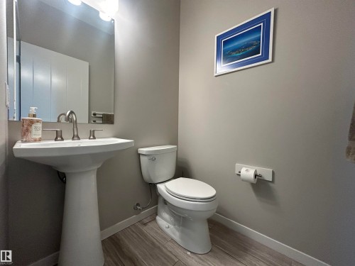 The powder room features a pedestal sink with a chrome faucet, a toilet, and wood-look flooring - 5333 21A Avenue, Edmonton, AB - Indoor Photo Showing Bathroom