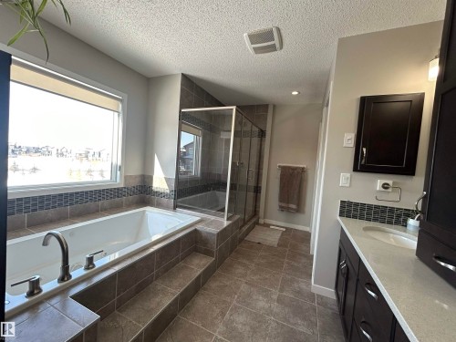 This bathroom features a spacious bathtub with a tiled surround, a separate glass-enclosed shower, and a vanity with a light-colored countertop - 5333 21A Avenue, Edmonton, AB - Indoor Photo Showing Bathroom