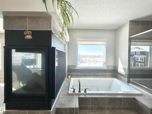 This bathroom features a built-in tub with a window view, surrounded by tiled surfaces - 5333 21A Avenue, Edmonton, AB - Indoor Photo Showing Bathroom