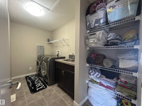 The laundry area features tile flooring, a dark-toned vanity with a sink, and an overhead light fixture - 5333 21A Avenue, Edmonton, AB - Indoor Photo Showing Laundry Room