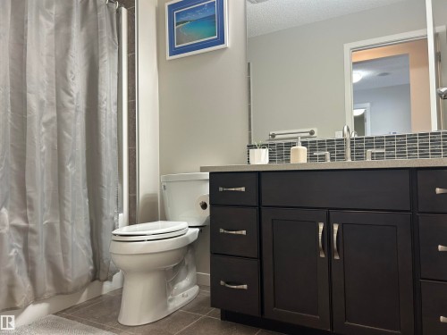 The bathroom features a dark wood vanity with a light-colored countertop, a subway tile backsplash, and a large mirror - 5333 21A Avenue, Edmonton, AB - Indoor Photo Showing Bathroom