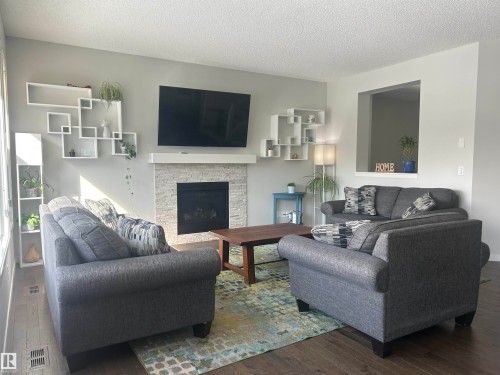 Living area featuring hardwood flooring, a fireplace with a natural stone surround, and an open pass-through window - 5333 21A Avenue, Edmonton, AB - Indoor Photo Showing Living Room With Fireplace