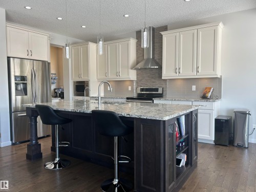 Kitchen featuring light-colored upper cabinetry, dark base cabinetry, a large kitchen island with a granite countertop, and stainless steel appliances - 5333 21A Avenue, Edmonton, AB - Indoor Photo Showing Kitchen With Upgraded Kitchen