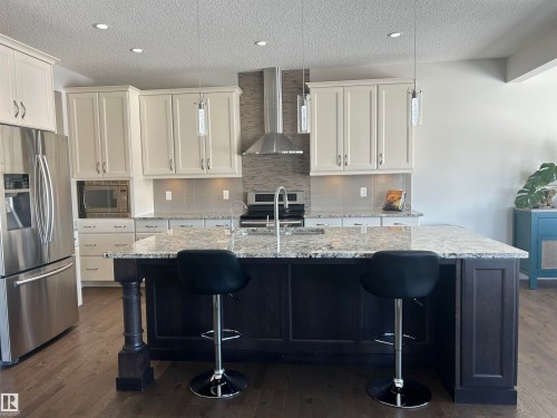 This kitchen features a large island with a light-colored granite countertop, dark wood cabinetry, and pendant lighting - 5333 21A Avenue, Edmonton, AB - Indoor Photo Showing Kitchen With Upgraded Kitchen