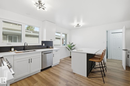 Kitchen with a breakfast bar, white cabinetry, tasteful backsplash, light wood-style flooring, and dishwasher - 2722 104A Street, Edmonton, AB - Indoor Photo Showing Kitchen