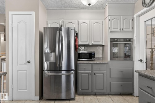 Kitchen featuring a stainless steel French door refrigerator, built-in wall oven, and light grey cabinetry with granite-style countertops - 5604 174 Street, Edmonton, AB - Indoor Photo Showing Kitchen