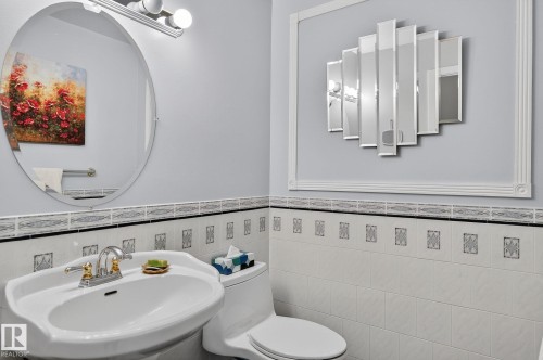 Bathroom featuring a pedestal sink with a chrome and gold-toned faucet, a wall-mounted oval mirror with an overhead light fixture, and decorative wall tiling - 5604 174 Street, Edmonton, AB - Indoor Photo Showing Bathroom