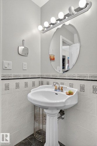 The bathroom features a pedestal sink with a chrome faucet, a large oval mirror, and a vanity light fixture with five bulbs - 5604 174 Street, Edmonton, AB - Indoor Photo Showing Bathroom