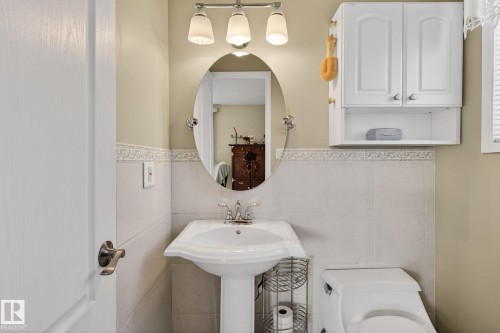 The bathroom features a pedestal sink, an oval mirror, and a wall-mounted cabinet for storage - 5604 174 Street, Edmonton, AB - Indoor Photo Showing Bathroom