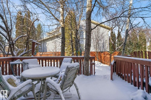 The property features a wooden deck with a railing, overlooking a yard with mature trees and a wooden fence - 5604 174 Street, Edmonton, AB - Outdoor With Deck Patio Veranda