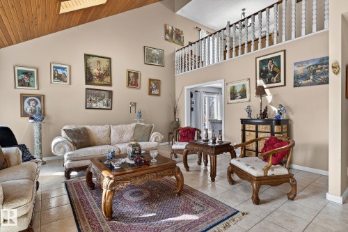 The living area features a vaulted wood-paneled ceiling with a skylight, a tiled floor, and a second-story interior balcony with white balusters - 5604 174 Street, Edmonton, AB - Indoor Photo Showing Living Room