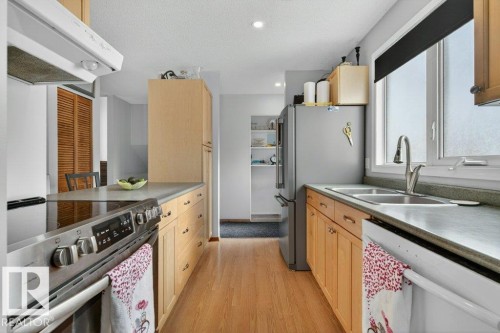 The kitchen features wood cabinetry, light-colored countertops, a double basin sink, and stainless steel appliances including a refrigerator and range - 2655 89 Street, Edmonton, AB - Indoor Photo Showing Kitchen With Double Sink