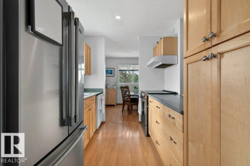 The kitchen features wood cabinetry, a stainless steel refrigerator, and hardwood flooring - 2655 89 Street, Edmonton, AB - Indoor Photo Showing Kitchen