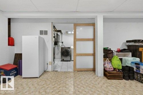 The property features a utility area with a white refrigerator and a separate laundry space with a washer and dryer, accessible through a wooden sliding door with frosted panels - 2655 89 Street, Edmonton, AB - Indoor Photo Showing Other Room