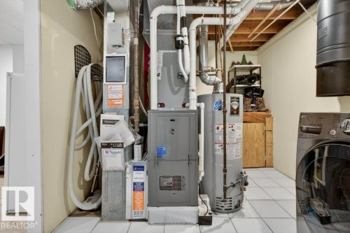 The utility area features a furnace, water heater, and a washer and dryer unit, set on white tiled flooring - 2655 89 Street, Edmonton, AB - Indoor