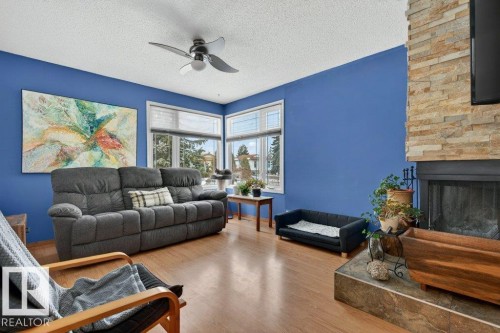 Living area featuring hardwood style flooring, a stone-faced fireplace with a hearth, and windows providing natural light - 2655 89 Street, Edmonton, AB - Indoor Photo Showing Living Room With Fireplace