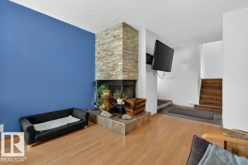 Living area featuring hardwood flooring, a stone-clad fireplace with a raised hearth, and a staircase with wooden treads - 2655 89 Street, Edmonton, AB - Indoor