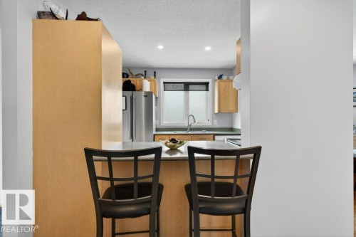 Kitchen featuring a breakfast bar with seating, light wood cabinetry, a stainless steel refrigerator, and a window above the sink - 2655 89 Street, Edmonton, AB - Indoor Photo Showing Kitchen