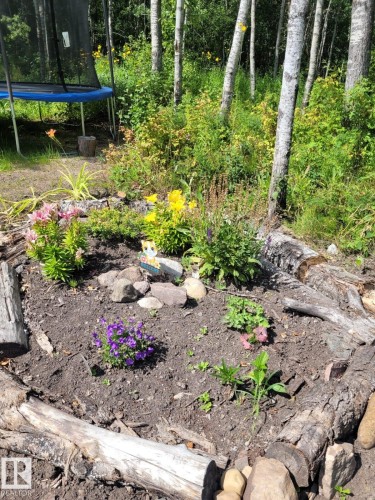 The property features a garden area with various plants and flowers, bordered by logs and rocks - 17 56110 Rge Road 13, Rural Lac Ste. Anne County, AB 