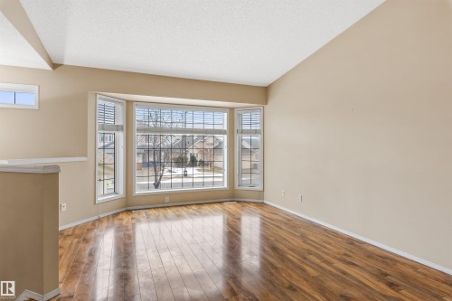 This spacious room features rich hardwood flooring and a large bay window with white blinds, offering abundant natural light - 1233 Ormsby Lane, Edmonton, AB - Indoor Photo Showing Other Room
