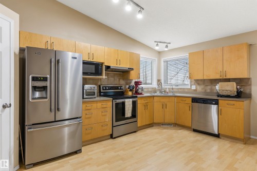 The kitchen features light wood cabinetry, stainless steel appliances, a tiled backsplash, and a double window above the sink - 1233 Ormsby Lane, Edmonton, AB - Indoor Photo Showing Kitchen