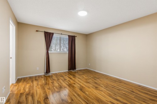 The room features wood-look flooring, neutral wall colors, and a window with blinds and dark curtains - 1233 Ormsby Lane, Edmonton, AB - Indoor Photo Showing Other Room