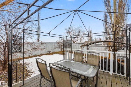 Outdoor deck area featuring a metal gazebo frame, a glass-top table with chairs, and a white wooden fence enclosing the yard - 1233 Ormsby Lane, Edmonton, AB - Outdoor With Deck Patio Veranda