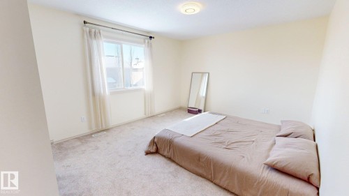 This bright room features a window with sheer curtains, neutral-toned carpet, and a ceiling light fixture, creating an inviting atmosphere - 1609 Hodgson Crest, Edmonton, AB - Indoor Photo Showing Bedroom