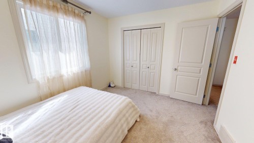 This bright room features a window with sheer curtains, a closet with bi-fold doors, and neutral carpeting - 1609 Hodgson Crest, Edmonton, AB - Indoor Photo Showing Bedroom