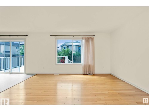 This bright room features hardwood flooring, a large window, and sliding glass doors that open to a balcony - 1609 Hodgson Crest, Edmonton, AB - Indoor Photo Showing Other Room