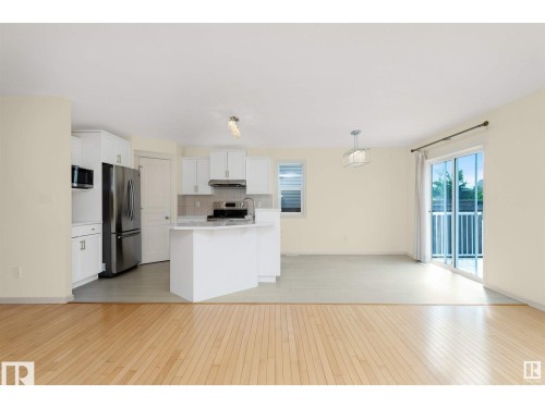 This property features light-colored hardwood flooring, a kitchen with white cabinetry and stainless steel appliances, and a sliding glass door leading to a balcony - 1609 Hodgson Crest, Edmonton, AB - Indoor Photo Showing Kitchen