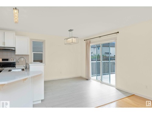 The property features an open-concept living area with light-colored flooring, a modern kitchen with white cabinetry, and a sliding glass door leading to an outdoor deck - 1609 Hodgson Crest, Edmonton, AB - Indoor Photo Showing Kitchen
