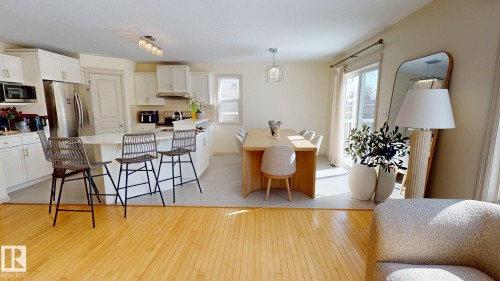 Open concept living area featuring hardwood flooring, a kitchen with white cabinetry and stainless steel appliances, and a dining area with a light wood table - 1609 Hodgson Crest, Edmonton, AB - Indoor