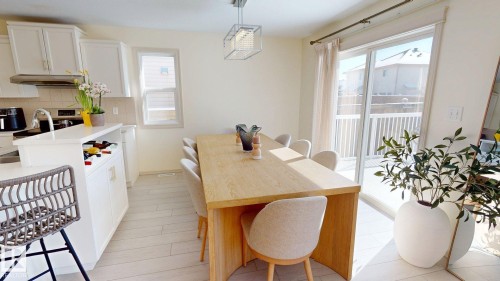 Bright dining area featuring a light wood table, upholstered chairs, and a contemporary light fixture, with sliding glass doors opening to an exterior deck - 1609 Hodgson Crest, Edmonton, AB - Indoor