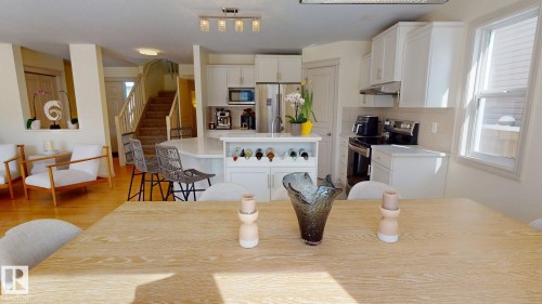 Open concept living space featuring hardwood floors, a kitchen with white cabinetry and stainless steel appliances, and a staircase with wooden treads - 1609 Hodgson Crest, Edmonton, AB - Indoor