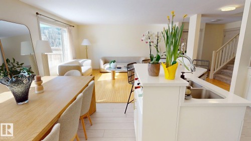 Well-lit open concept living space featuring light wood flooring, white walls, and a kitchen island with a sink and a high arc faucet - 1609 Hodgson Crest, Edmonton, AB - Indoor