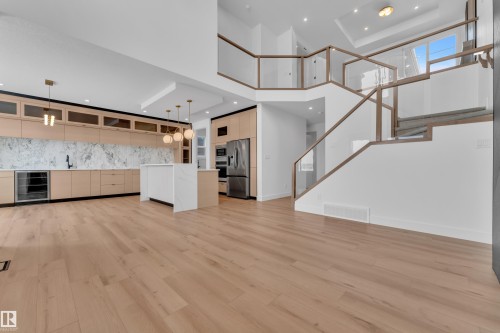 The open-concept living area features light wood flooring, a kitchen with light wood cabinetry, a white island, and a stainless steel refrigerator - 503 Creekside Bay, Leduc, AB - Indoor