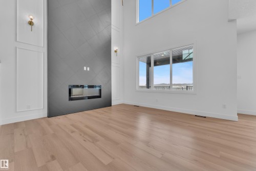 Living area featuring light wood flooring, a modern fireplace with a tiled surround, and large windows providing natural light and views - 503 Creekside Bay, Leduc, AB - Indoor With Fireplace