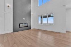 Living area featuring light wood flooring, a modern fireplace with a tiled surround, and large windows providing natural light and views - 