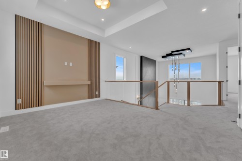 This spacious interior area features light gray carpeting, a decorative wall panel with a built-in shelf, and a contemporary light fixture - 503 Creekside Bay, Leduc, AB - Indoor Photo Showing Other Room