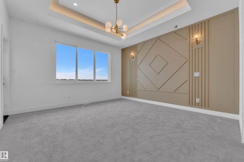 Spacious room featuring light grey carpeting, a large window, and a decorative wall with sconces - 503 Creekside Bay, Leduc, AB - Indoor Photo Showing Other Room