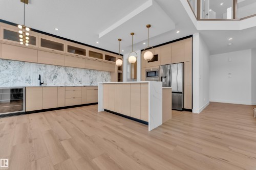 The kitchen features light wood cabinetry, a white marble backsplash, and a central island with a white countertop - 503 Creekside Bay, Leduc, AB - Indoor Photo Showing Kitchen