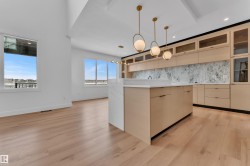 Open concept living space featuring light hardwood flooring, a contemporary kitchen island with a white countertop and waterfall edge, and custom cabinetry with glass-fronted upper cabinets - 