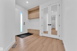 Entryway featuring light hardwood flooring, a modern front door with a vertical glass insert, and built-in wooden cabinetry and bench - 