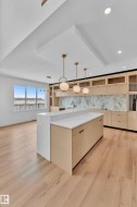 This modern kitchen features light wood flooring, a spacious island with a white countertop, and contemporary pendant lighting - 